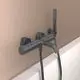 Schwarze Wandarmatur von Ideal Standard mit Handbrause, Brauseschlauch und Wandhalter. Installation über einer weißen Badewanne an einem beige gefärbten Wandbereich.